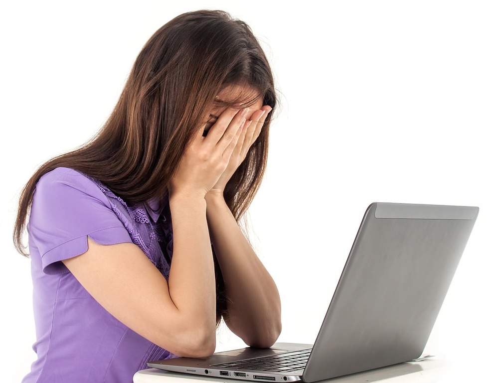 Billede af fortvivlet kvinde siddende ved computer med hoved skjult af hænder